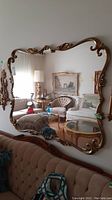 Full view of ornate metal framed mirror mounted on wall reflecting living room furniture and paintings.