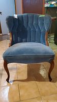 Front view showing blue tufted velvet upholstery and wooden frame of vintage parlor chair