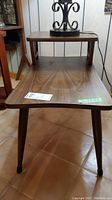 Photo of mid-century modern two-tiered side table showing wood grain surface, tapered legs, and partial view of decorative sides.