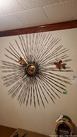 Full front view of the starburst wall sculpture hung on beige wall showing the overall shape and size