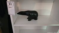Front and side view of black stone bear sculpture on white shelf.