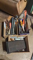 Three cardboard boxes filled with various hand tools including wrenches, pliers, files, and a hammer.