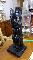 Front right angle view of black hematite-like totem sculpture showing side and front detail with mother of pearl eye inlaid.