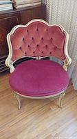 Front view of the vintage wooden chair showing tufted red velvet seat and backrest with cream-colored carved frame.
