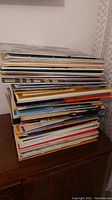 Stack of approximately 35 vinyl record albums piled on top of a cabinet, showing thickness and quantity of collection.