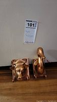Both brass wall hangers displayed side by side on a wooden surface against a white background with lot label.