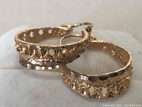 Close-up image showing the design and texture of the 10k gold hoop earrings with cut-out elements and hammered finish.