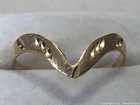 Close-up photo showing the V-shaped curve design and engraved texture on the gold band.