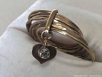 Front view of multi-band gold ring with dangling heart charm and clear stone