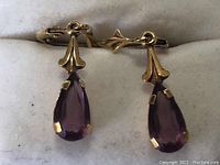 Front view of both earrings laid flat showing gold hooks and purple teardrop stones
