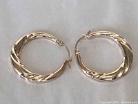 Pair of gold hoop earrings laid flat on light background