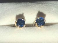 Front view of both earrings resting on a padded display surface, showing deep blue round stones and gold prongs