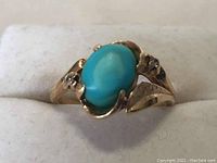Front view of yellow gold ring with oval green cabochon stone aboard white display