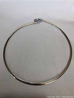 Full view of the choker necklace laid flat on white backdrop, showing the gold and silver metal chain in circular form.