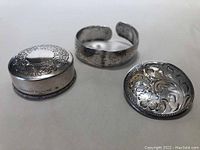 Sterling silver pin jar, cuff bracelet, and brooch on flat surface.