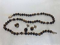 Full view of necklace, heart-shaped charm, and stud earrings laid out on white surface