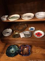 Shelf with majority of ashtrays showing a variety of ceramic, glass, metal pieces with assorted prints and styles.