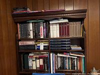 Full view of a wooden bookshelf filled with diverse hardback books mostly on history, art and garden.