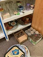 Wide view of white shelving with multiple canning jars, metal trays, one glass tray, coordinating lid boxes, and wax packaging.