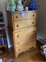 Front view of the wooden chest of drawers showing 5 drawers and round wooden knobs. Scratches and usage marks visible. Decorative vases on top (not included).