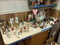 Wide view of Christmas figurines including angels, Santas, and assorted holiday characters displayed on a countertop.