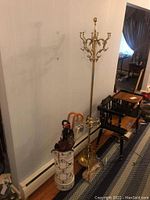 Photo showing the brass coat rack and the ceramic umbrella stand placed side by side with some umbrellas inside the stand.