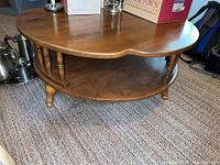 Full view of round wooden coffee table with lower shelf and turned legs.
