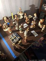 Wide view of multiple Hummel figurines and porcelain dishes on a table, including child figures and animal themes.