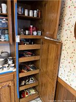 Open kitchen cabinet with drawers pulled out showing various kitchen utensils including wooden spoons, measuring tools, cutters and gadgets