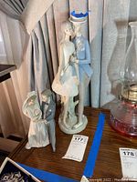 Both Lladro porcelain figurines side by side, showing bride and groom couples in wedding attire next to an oil lamp.