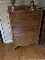 Front view of oak chest showing five drawers with brass handles and keyhole.