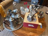 Photo showing entire lot on wooden table including pewter coffee pots with wood handles on a large pewter tray and Baldwin Georgetown candlesticks packaged in box.