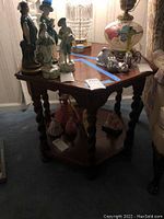 Front and side angle showing the hexagonal wooden two-tier table with spiral legs, medium brown wood, some surface scratches, decorative figurines on top and bottom shelf are not included.