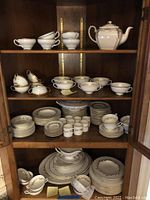 Full set of china including teapot, cups, saucers, plates and bowls arranged inside cabinet showing overall lot contents
