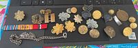 All items displayed on black surface showing diverse WWII US military insignia, buttons, ribbons, and a chain bracelet