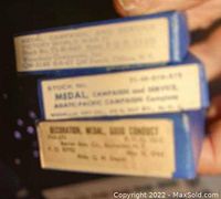 Photo of labels on blue boxes showing the medal types: Medal, Campaign and Service, Asiatic-Pacific Campaign, and Good Conduct Medal, with stock and issue numbers.