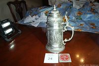 Left front angle view of the WMF German pewter beer stein on a wood table, showing detailed relief images and handle.