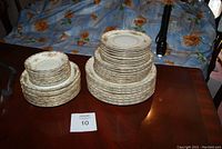 Photo showing stacked dinner plates, salad plates, and fruit nappies in white china with floral design and gold edges