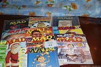 Image showing ten MAD magazines arranged on a surface with varied colorful covers including a Santa Claus cover and a cover featuring a cartoon boy in a blue shirt.