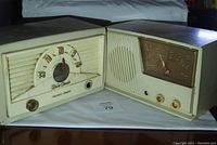 Two vintage radios side by side on white cloth showing front faces with dials and speaker grilles.