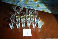 Photo of all 21 assorted glass and crystal shot and liqueur glasses arranged on a wooden table.