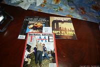 Three magazines on a wooden table showing the front covers. Time magazine in front, People magazine on right, commemorative magazine on left.