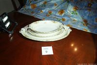 Three white china pieces with floral and gold trim stacked, showing ornate edges and different sizes of platters and bowl.