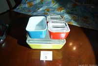 Stacked view of 4 Pyrex dishes in yellow, blue, and two small red and blue square dishes with clear lids.