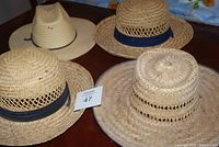 Four straw hats shown from top front view on wooden surface with white tag number 47