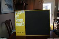 Yellow Tail advertising chalk board featuring large yellow panel with 'PLAY BY YOUR RULES.' text and adjacent chalkboard area.