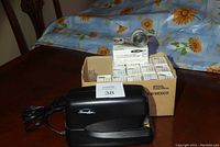Black Swingline stapler model 270, metal staple remover on top of box full of staple cartridge boxes