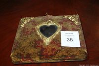 Front cover of antique velvet picture album showing embossed gold corners and heart-shaped window.