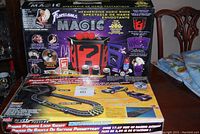 Photo showing the Fantasma Magic set box with images of magic tricks props and the Artin race track set below with two slot cars.