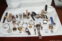 Overview of assortment of 23 men's and ladies' wristwatches and pocket watches displayed on white cloth, various bands and styles.